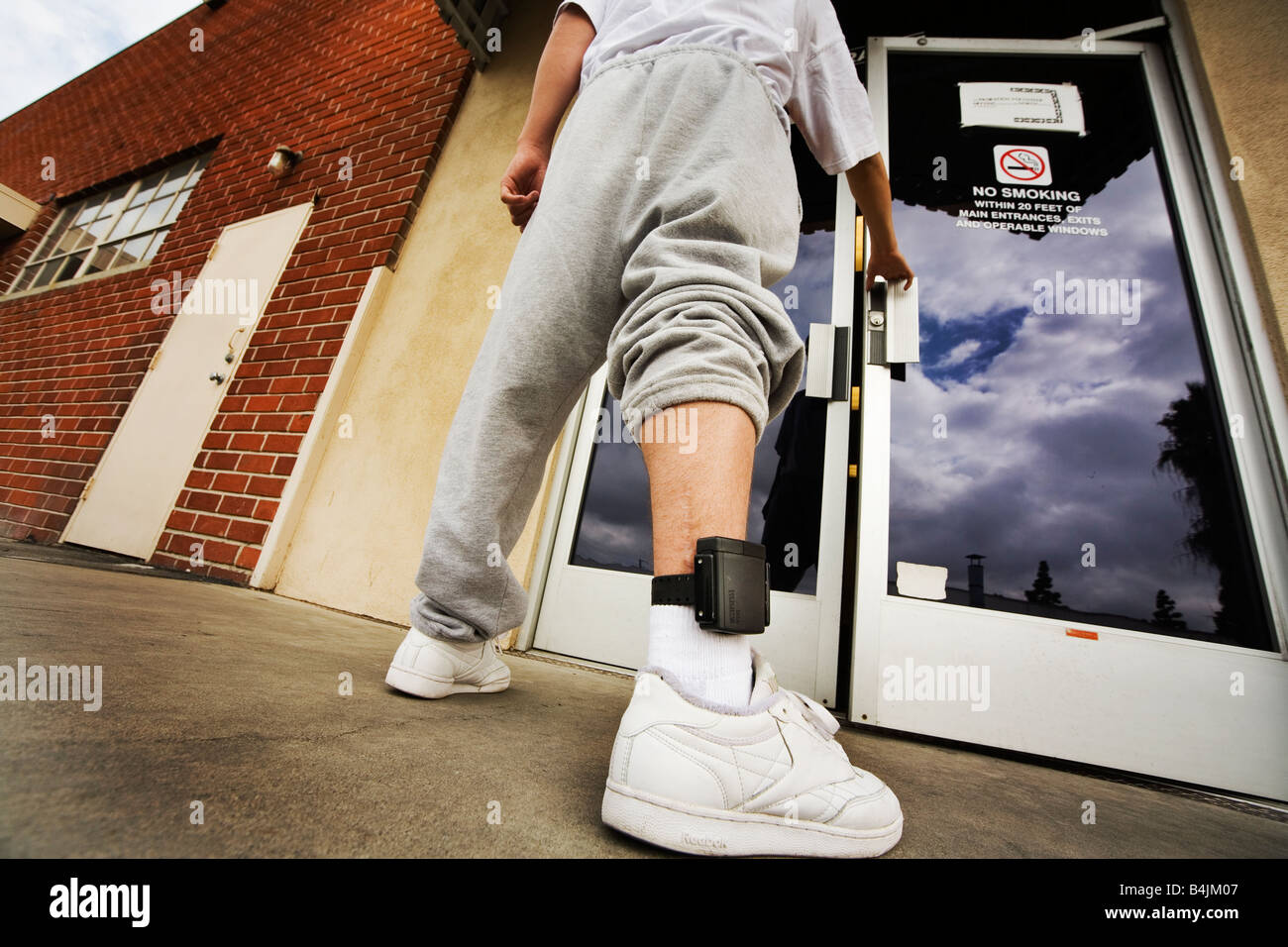 Wearing an electronic ankle monitor a teenage offender enters a county parole facility in Santa Ana CA Stock Photo