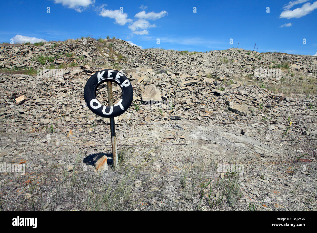 Barbed wire fence with tire sign painted keep out near Pincher Creek