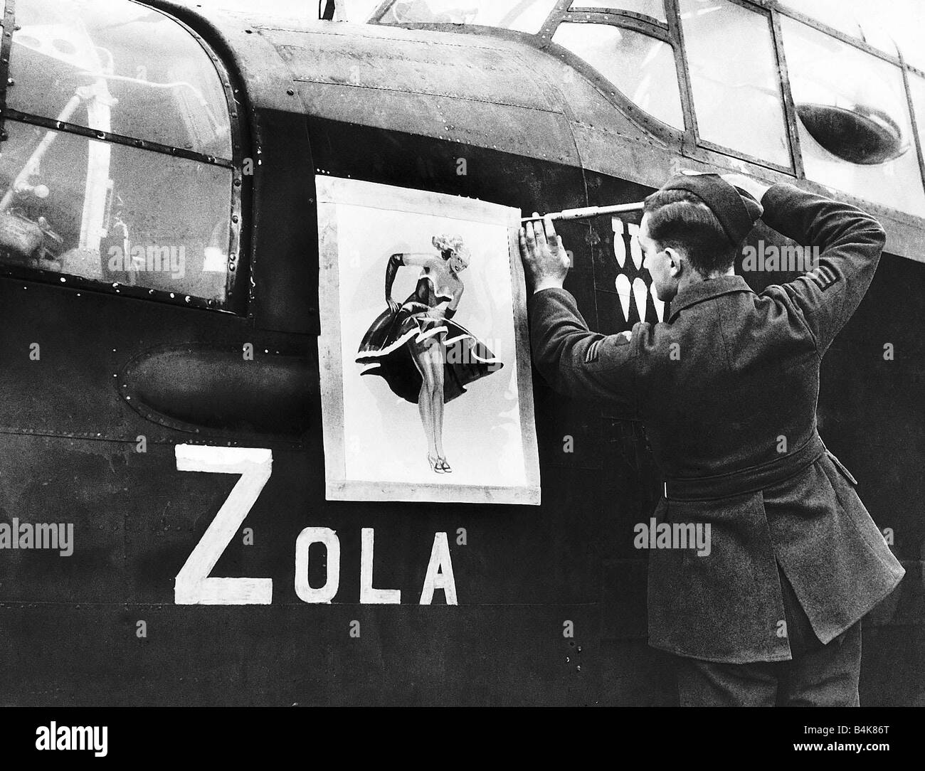 A Lancaster bomber crewman screws on a nose art painting of Zola on to the side of the aircraft for good luck during WW2 1942 Stock Photo