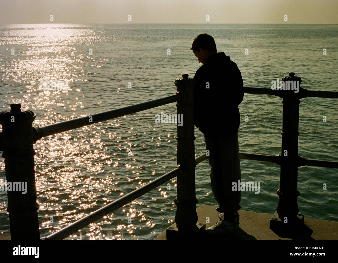 Silhouette of a boy looking out to sea from quayside. Stock Photo