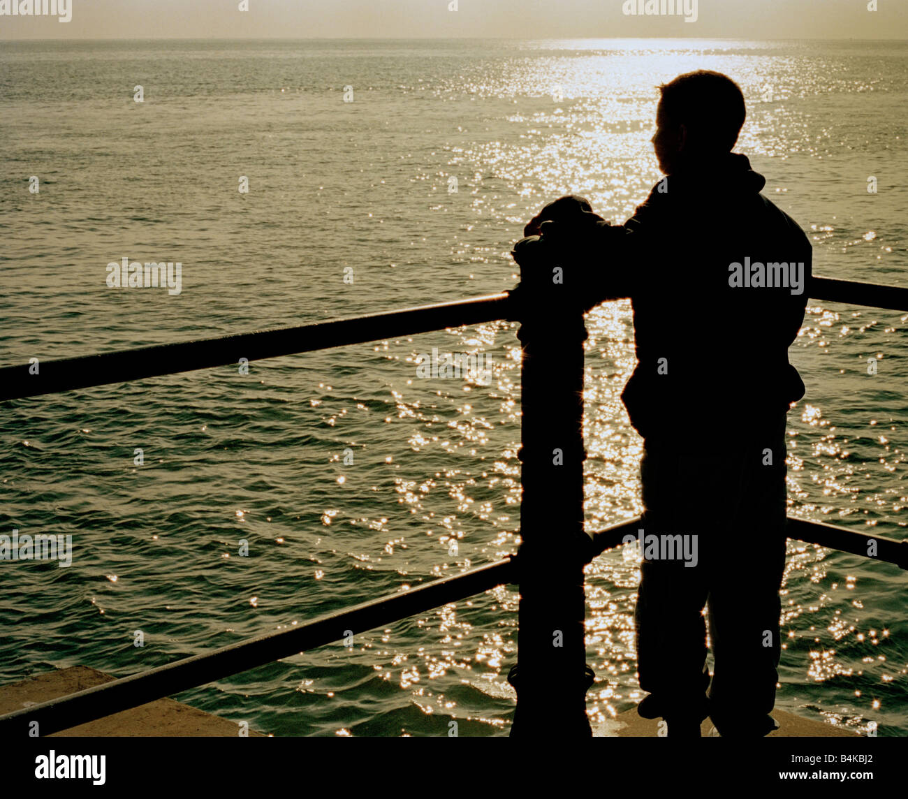 Silhouette of a boy looking out to sea from a quayside. Stock Photo