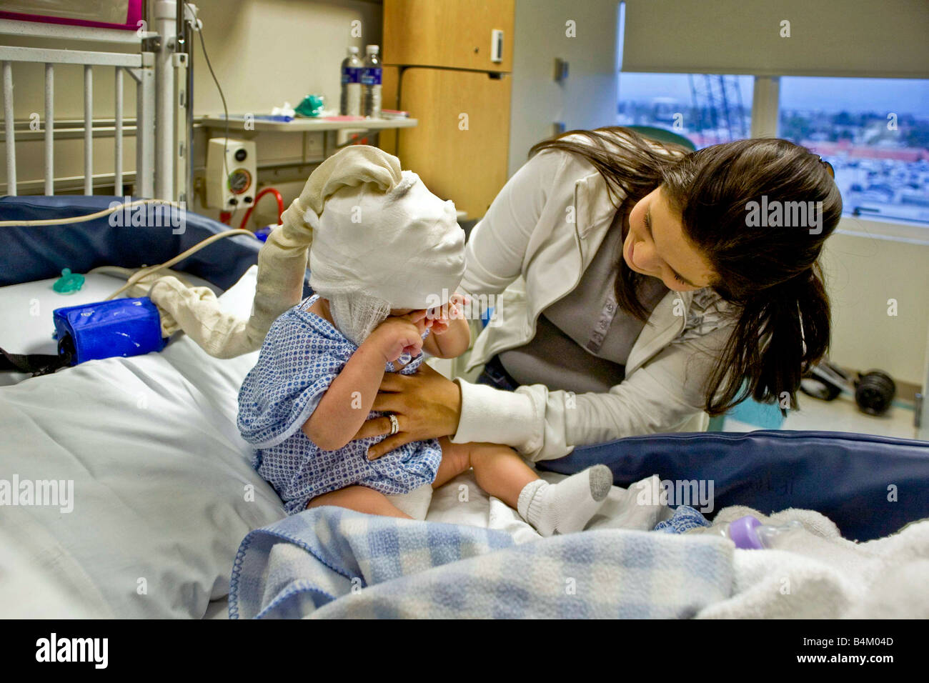 In a California hospital a mother cares for her infant son suffering from spinal bifida Note condition monitoring EEG cap Stock Photo
