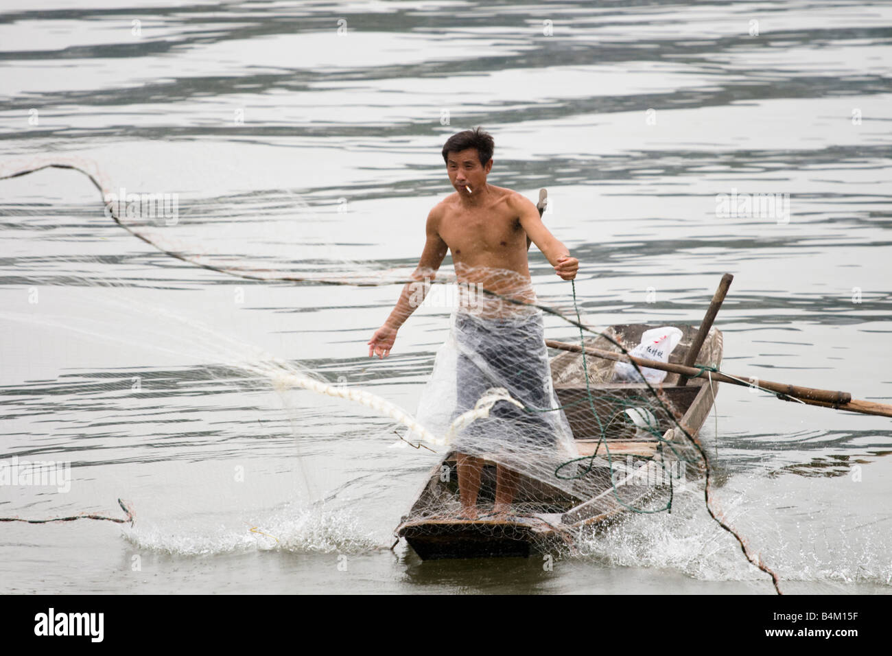A Chinese man throwing a fishing net off a small traditional boat