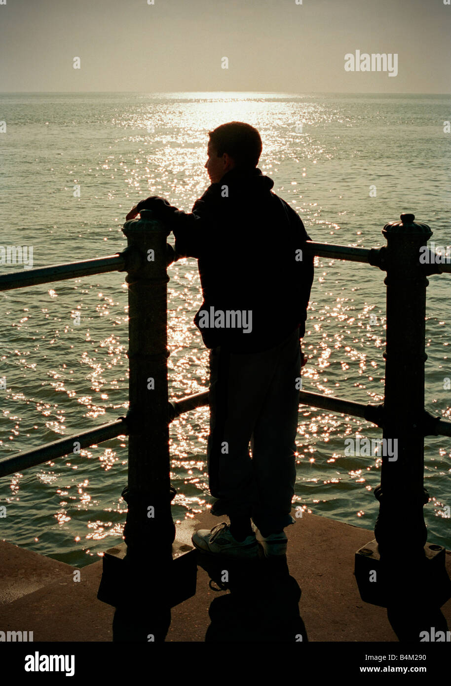 Silhouette of a boy looking out to sea from quayside. Stock Photo