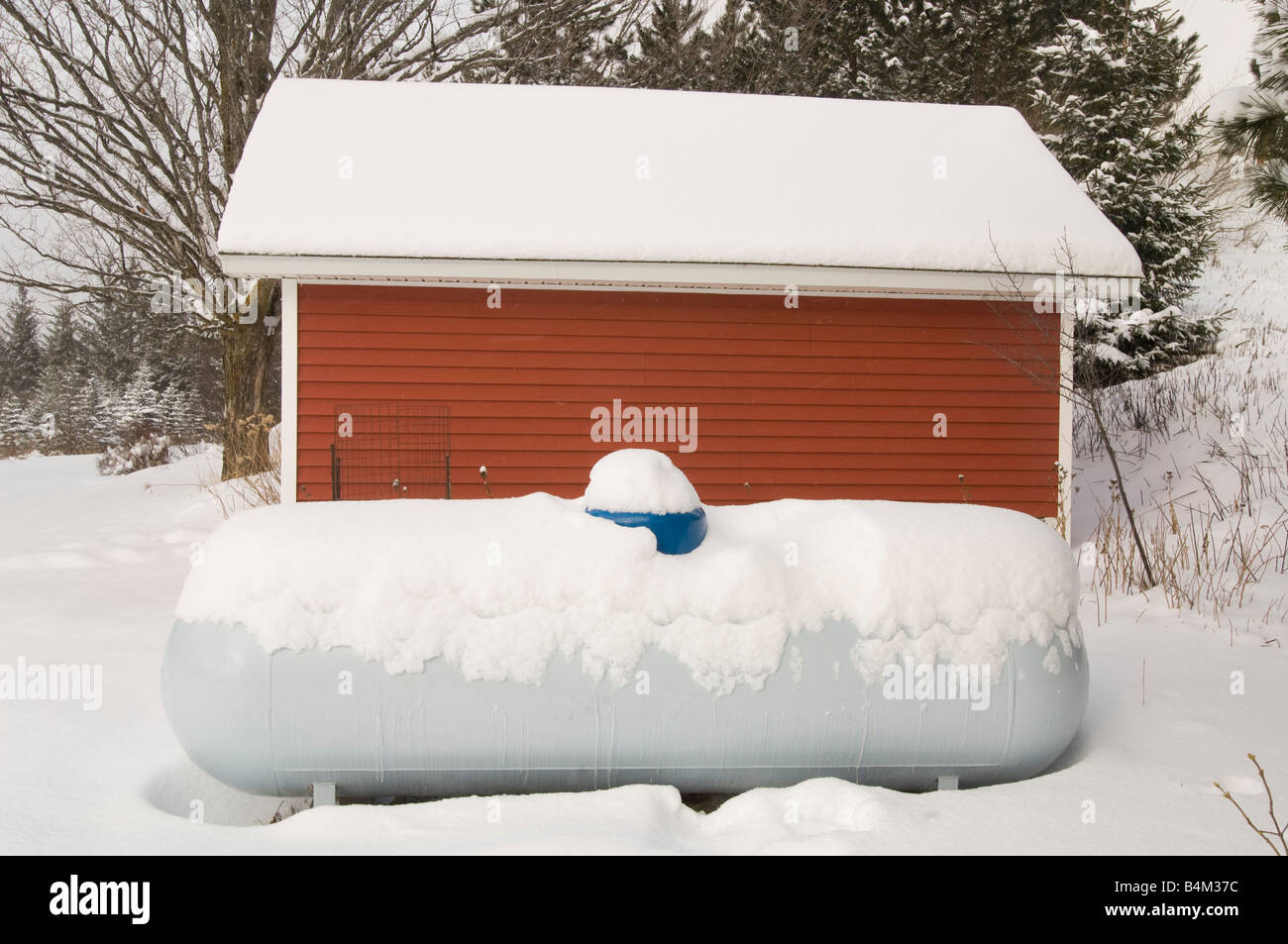 A snow covered propane LP tank and red farm building during winter