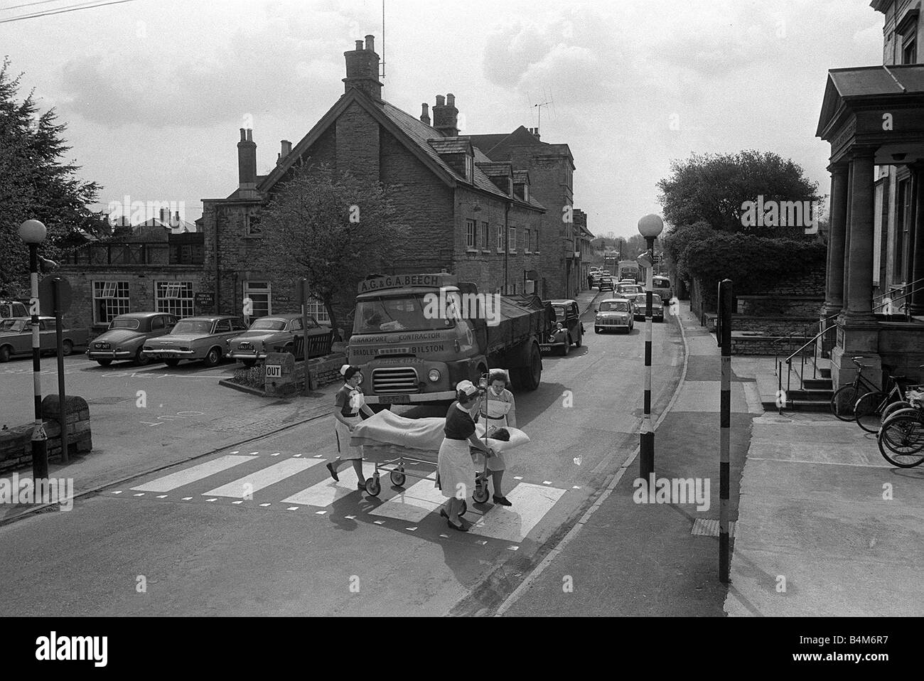 Student nurse Anne Luce Nurse Betty de Silva glasses and Sister Ruth Miller taking Emergency Patient with Blood drip across a busy road from one side of Cirencester Memorial Hospital to the other The Cirencester Memorial Hospital is divided by a main road 1966 Stock Photo