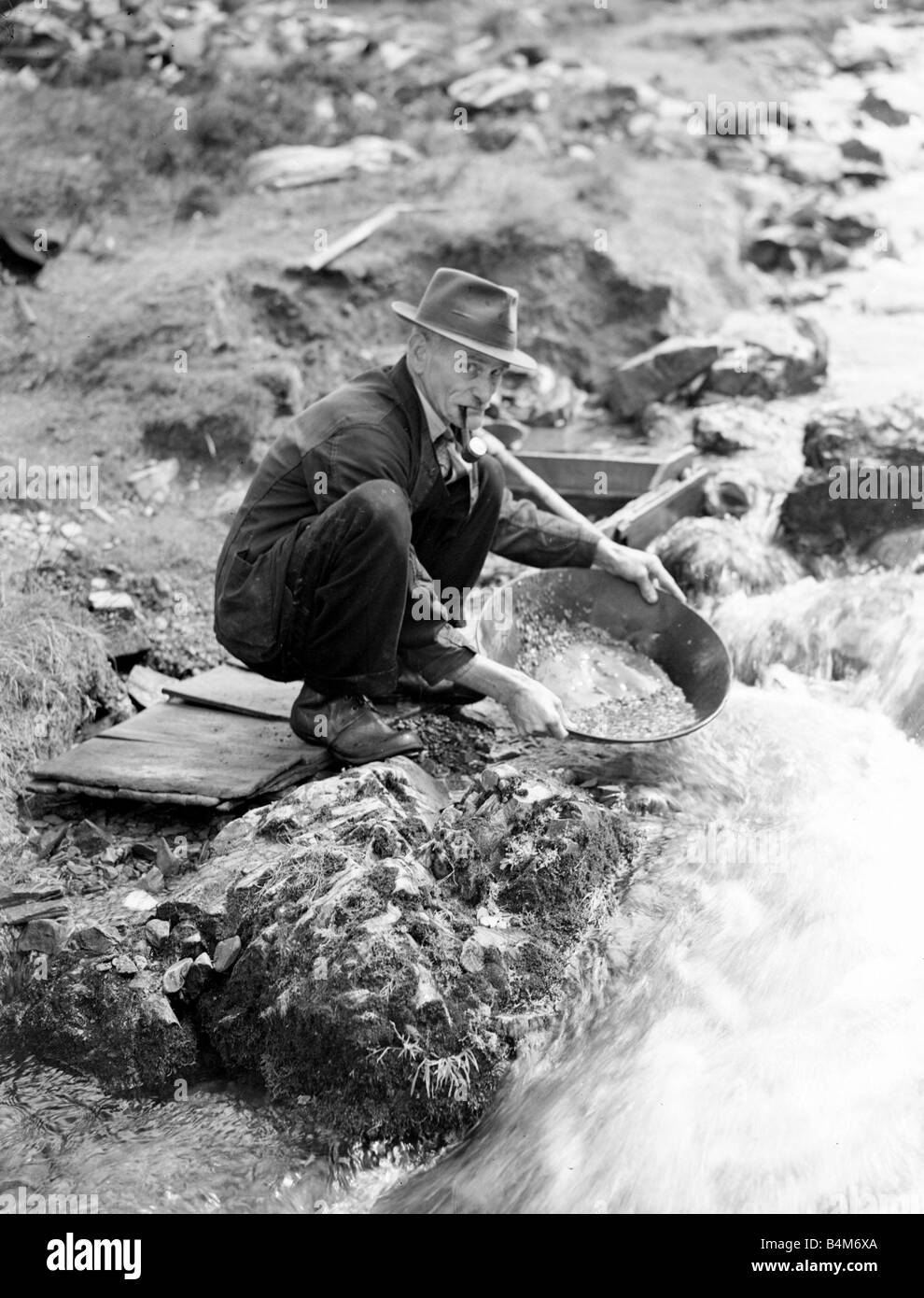 Scottish Gold Prospect man smoking pipe by a river bank Circa 1920 Stock Photo