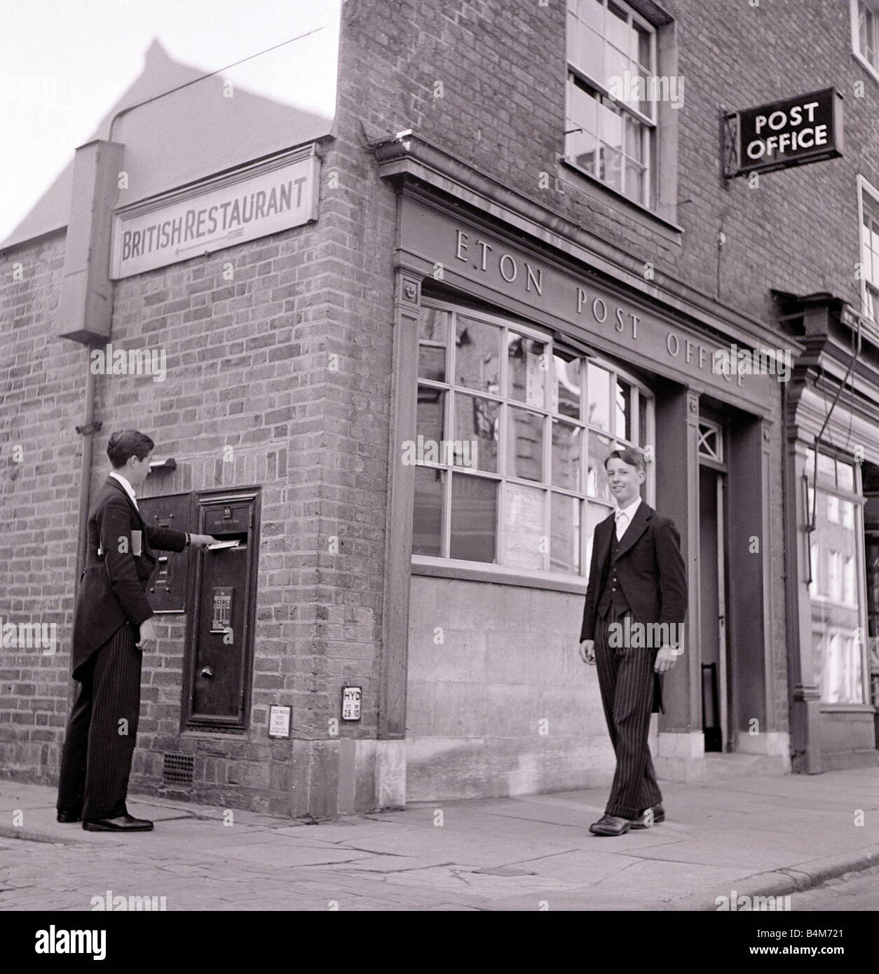Eton schoolboy walks past Eton Post Office whilst another boy posts a