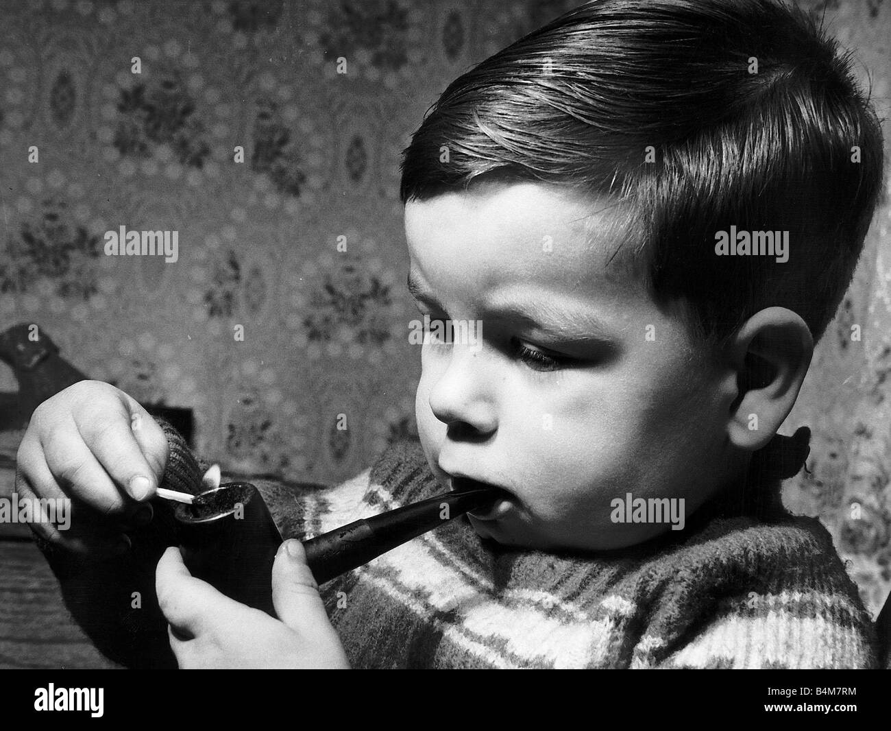 Smoking at an early age for 2 year old Hugh Condron Would you let your two year old son smoke and drink Chubby Hugh Condron of Muirmadkin Road Bellshill North Lanarkshire Scotland who was two in September 1962 does both Hugh s drinking career started at the Glasgow Fair holiday when his Uncle Mr Tom Miller gave him a little taste of beer He gulped it down and held out his glass for more It was also through his uncle that Hugh acquired his taste for the pipe Mr Miller laid down his lit pipe for a moment and before he could pick it up again young Hugh had it in his mouth taking his first puff Stock Photo