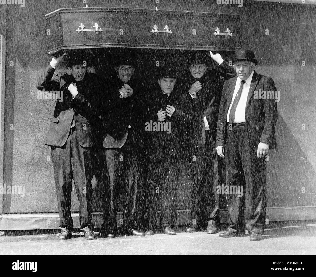 Furneral Directors using a coffin to stay dry as it pours down with rain Circa 1990 Stock Photo