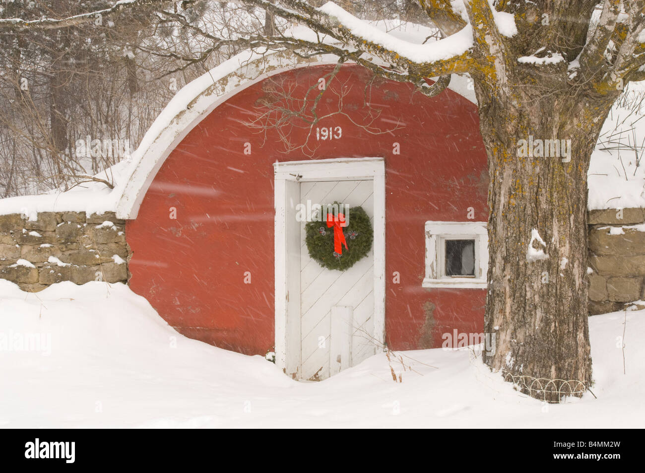 An old red root cellar with a Christmas wreath during a snowstorm Stock Photo