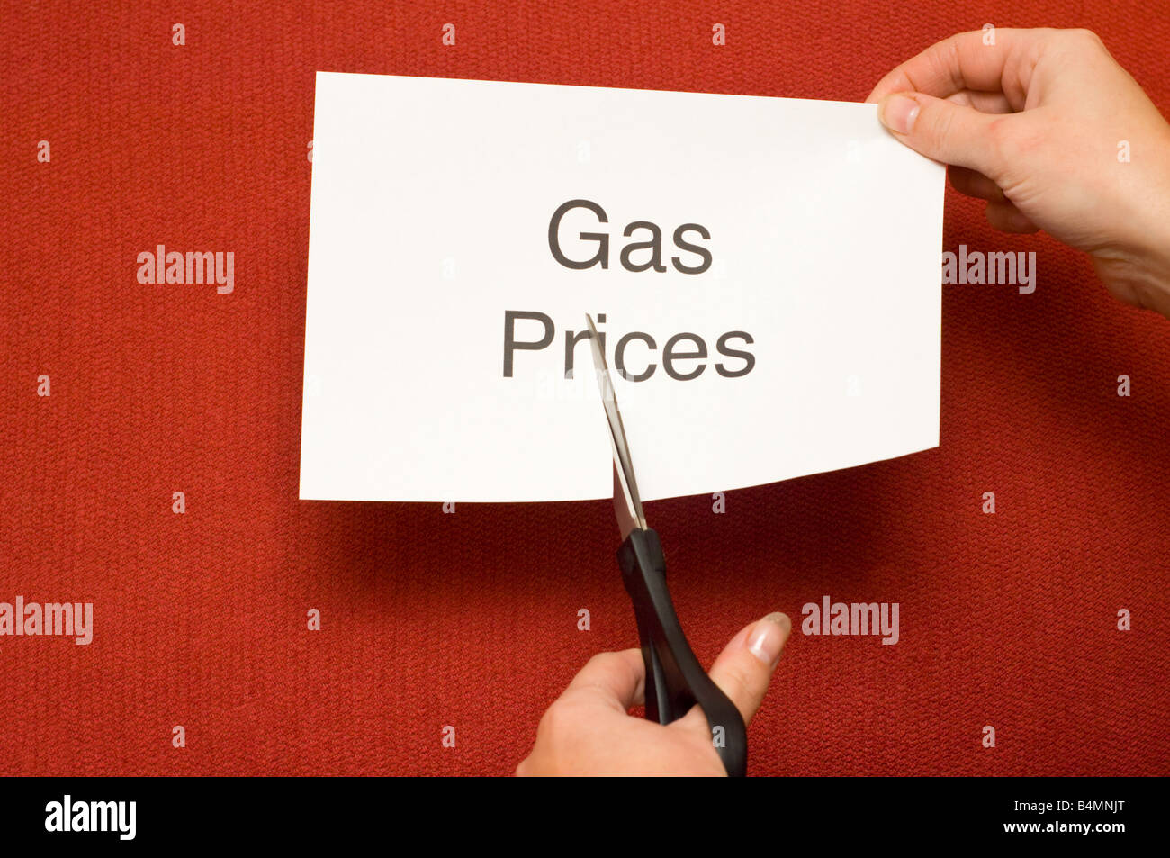 Picture of person cutting a piece of paper with 'Gas prices' written on it using a pair of scissors Stock Photo