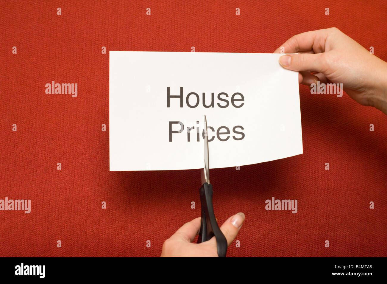Picture of person cutting a piece of paper with 'House prices' written on it using a pair of scissors Stock Photo