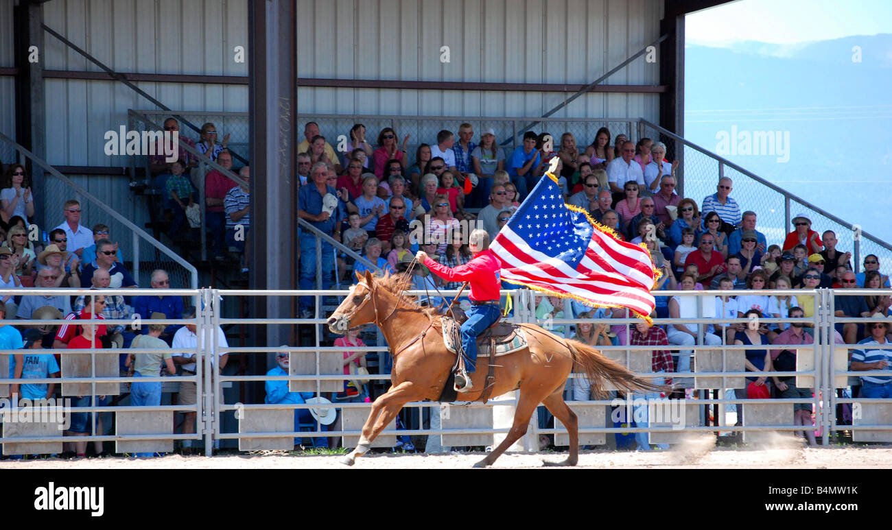 Cowboy carrying an American flag while riding on a horse at a rodeo Stock Photo