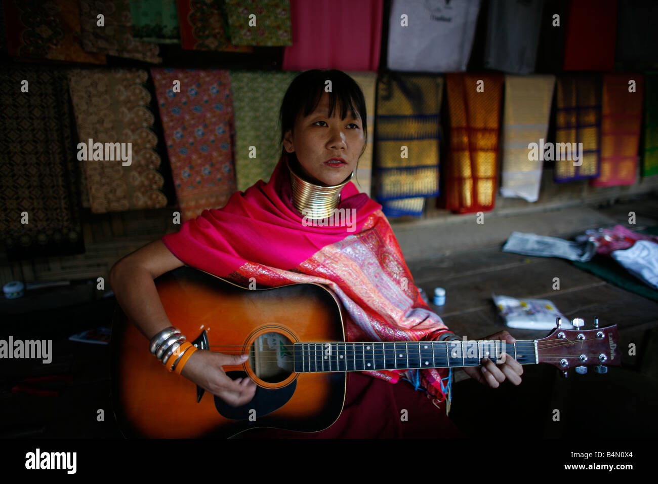 A Longneck woman plays a guitar Approximately 300 Burmese refugees in Thailand are members of the indigenous group known as the Longnecks The largest of the three villages where the Longnecks live is called Nai Soi located near Mae Hong Son City Longnecks wear metal rings on their necks which push the collarbone done and extend the neck They are a tourist attraction Tourists visit Nai Soi to take pictures of the Longnecks and buy their handicrafts The villages are criticized by human rights organizations as human zoos Stock Photo