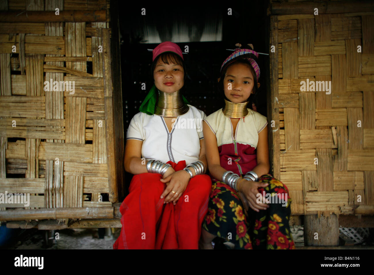 Two Longneck girls sitting outside a hut Approximately 300 Burmese refugees in Thailand are members of the indigenous group known as the Longnecks The largest of the three villages where the Longnecks live is called Nai Soi located near Mae Hong Son City Longnecks wear metal rings on their necks which push the collarbone down and extend the neck They are a tourist attraction Tourists visit Nai Soi to take pictures of the Longnecks and buy their handicrafts The villages are criticized by human rights organizations as human zoos Stock Photo
