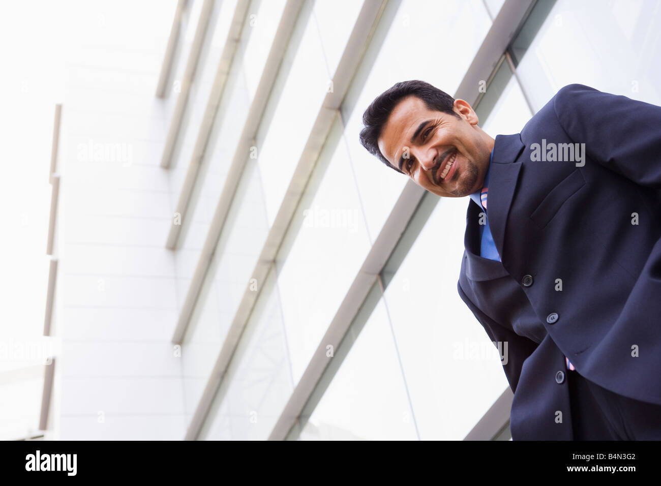 Businessman standing outdoors by building smiling (high key/selective ...