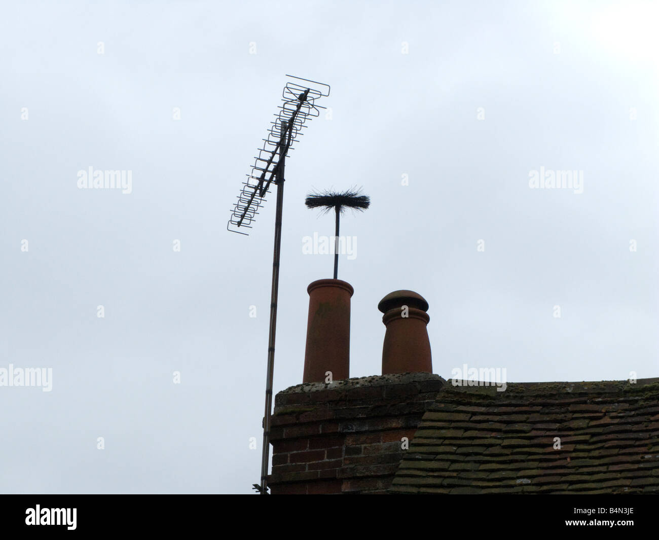 A Chimney Sweeps brush pops out of a house chimney Stock Photo