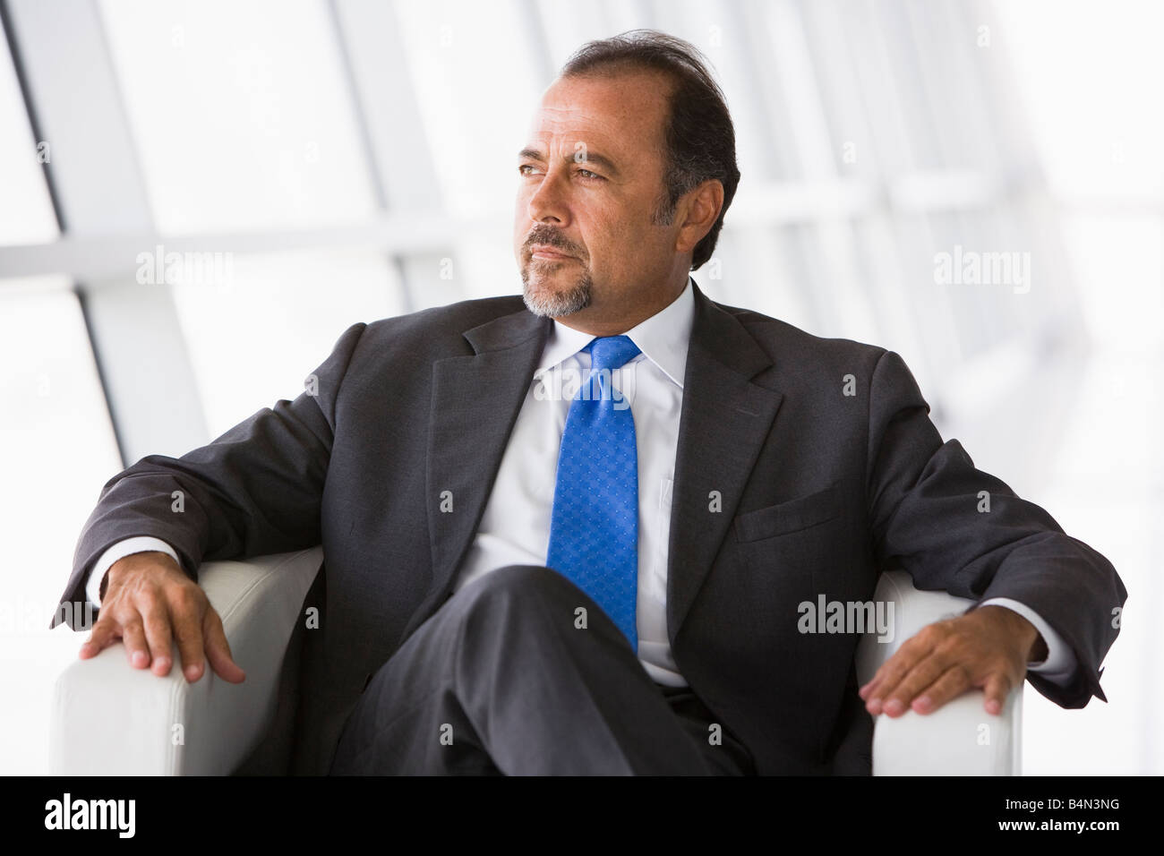 Businessman sitting indoors looking out window (high key/selective focus) Stock Photo