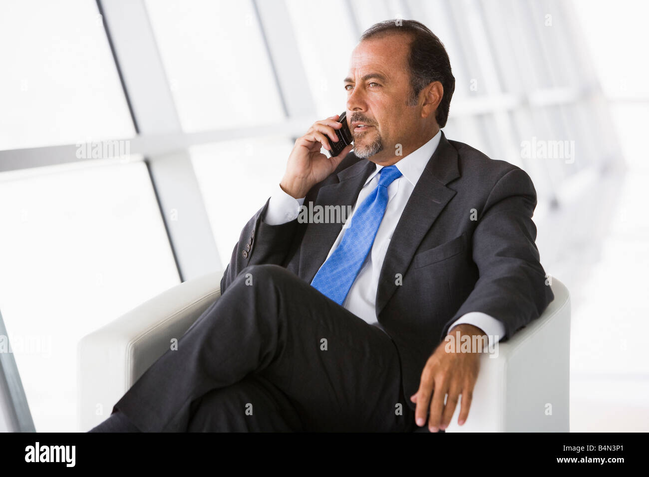 Businessman sitting indoors on cellular phone (high key/selective focus) Stock Photo