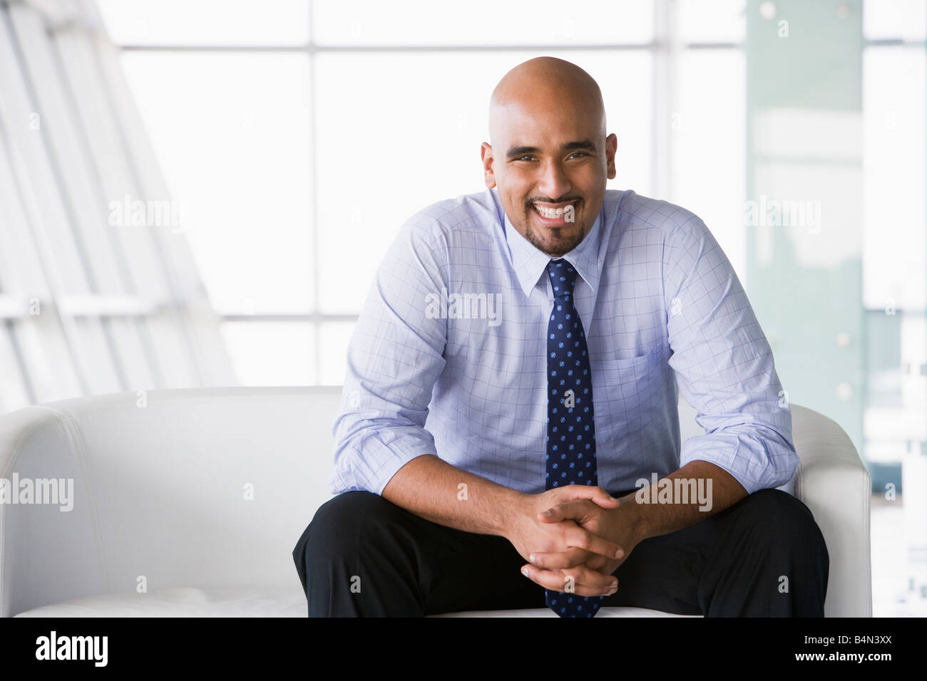 Businessman sitting indoors smiling (high key/selective focus) Stock Photo