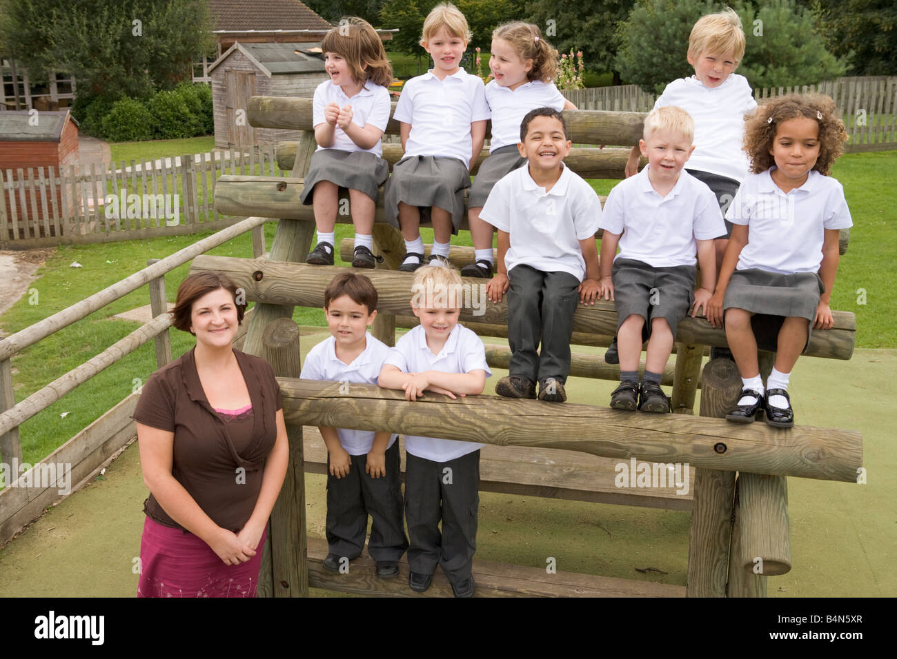 Students sitting outdoors on wooden structure with teacher standing beside them Stock Photo