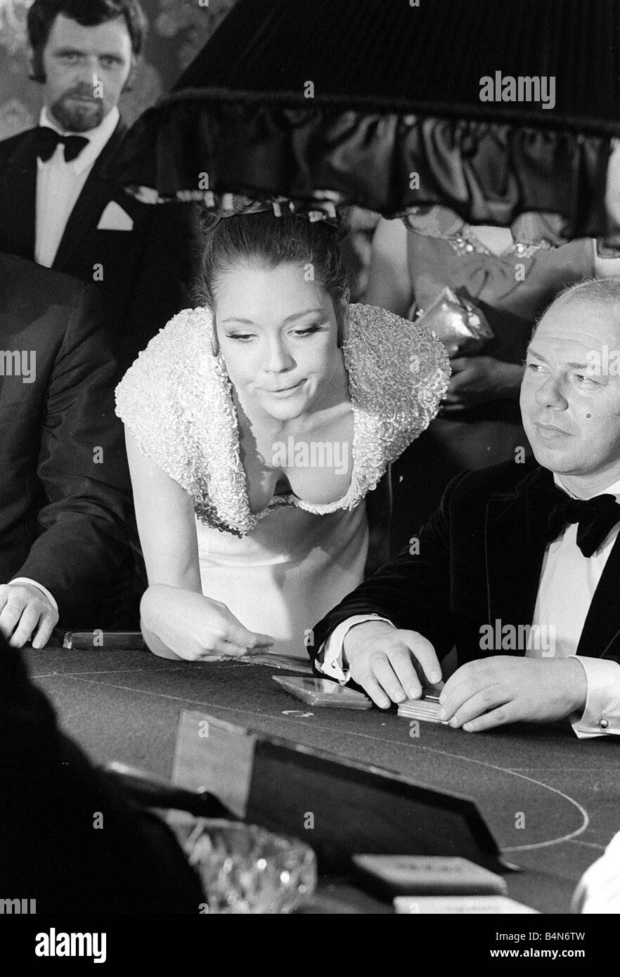 Diana Rigg in a low cut dress leans across the Black Jack table in a ...