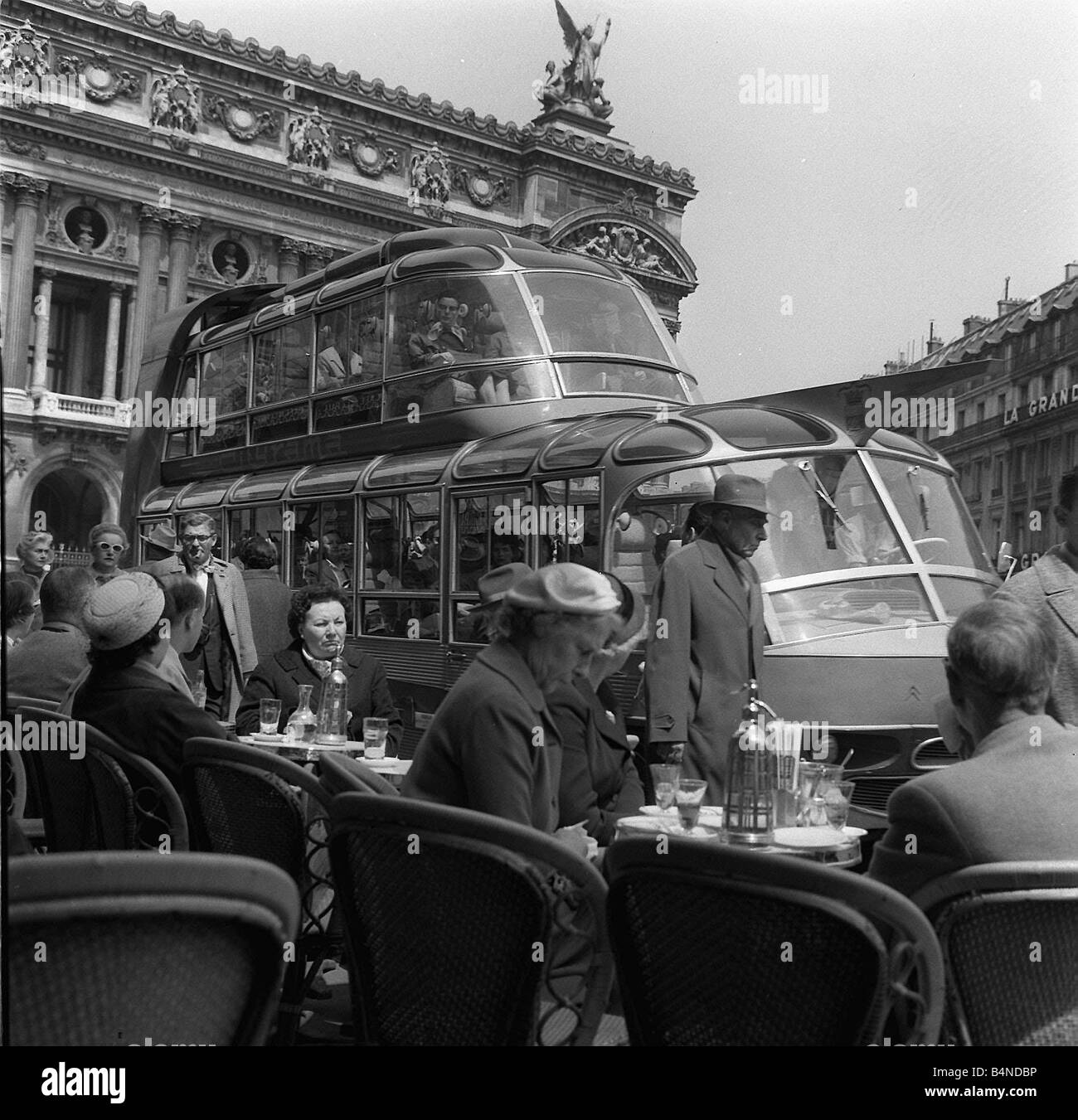 People sitting in front of the Opera Garnier Paris May 1960 on a cafe terrace with a bus tram behind them Stock Photo