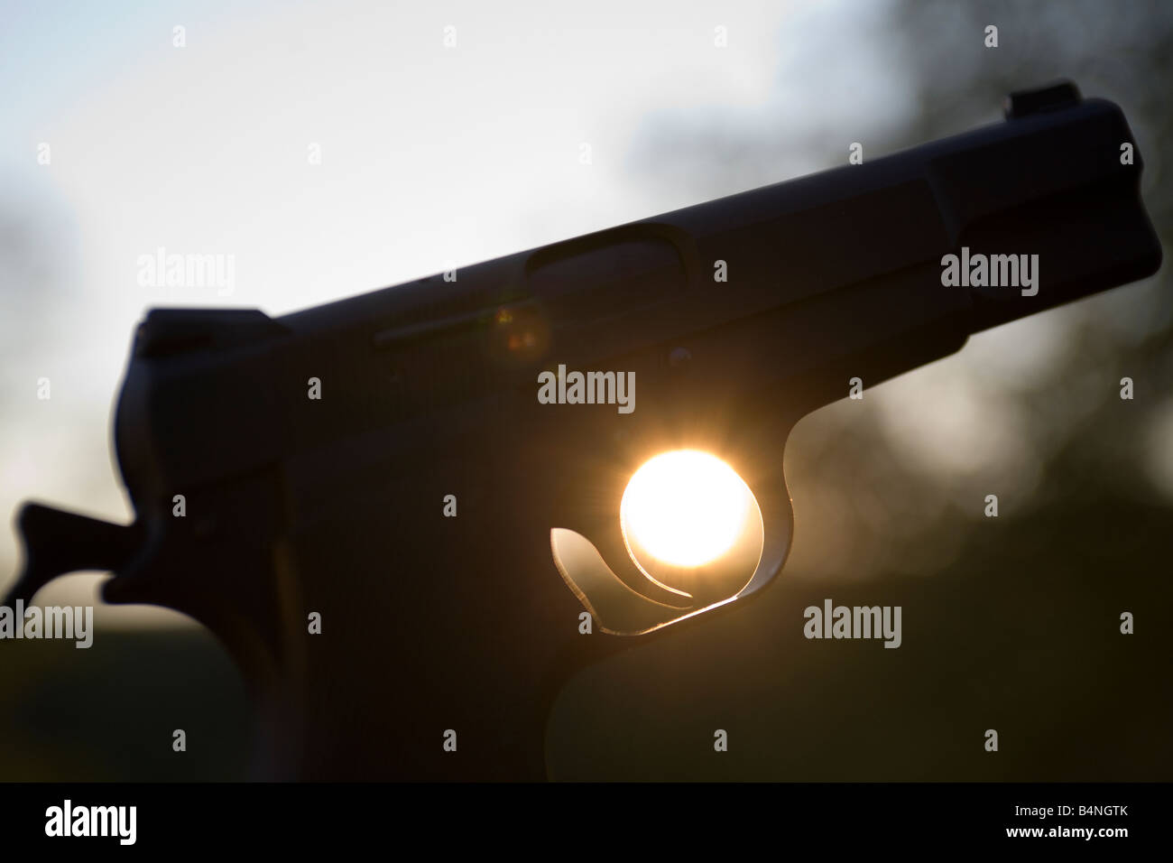 A handgun held against a setting sun A sunset peers through the finger grip of a handgun. Stock Photo
