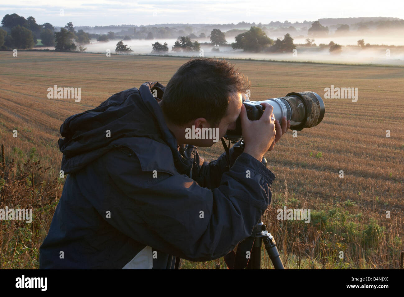 Photographer photographing the early morning mist with a long lens in the UK countryside Stock Photo