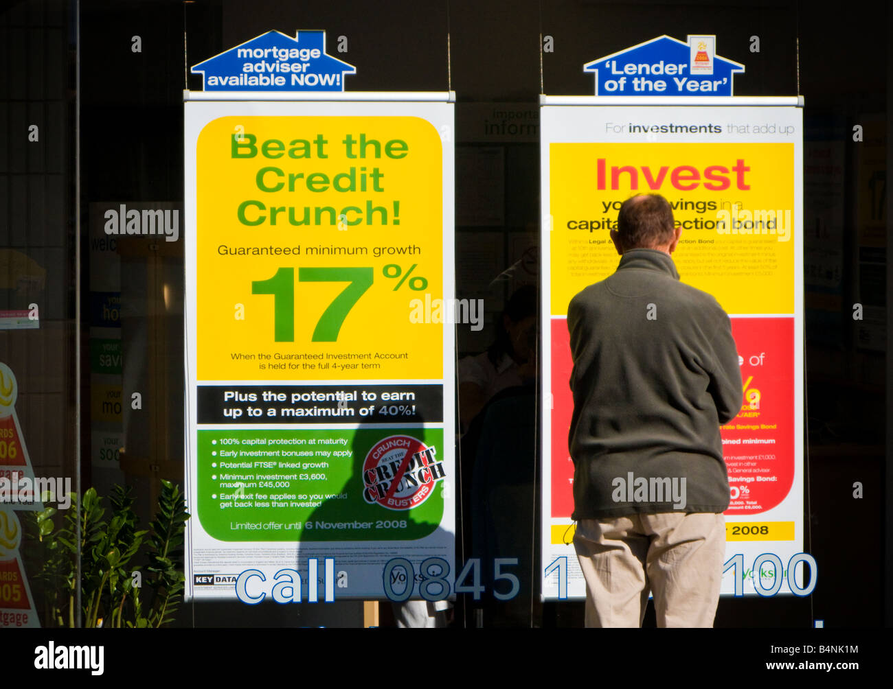 Man looks at poster in a bank building society window which promises high interest rates with their investment product UK Stock Photo