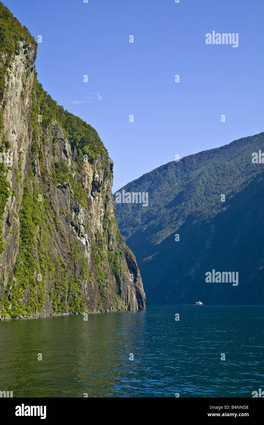 Sheer cliff on the southern side of Milford Sound with a tourist boat visible, giving the scale. Stock Photo
