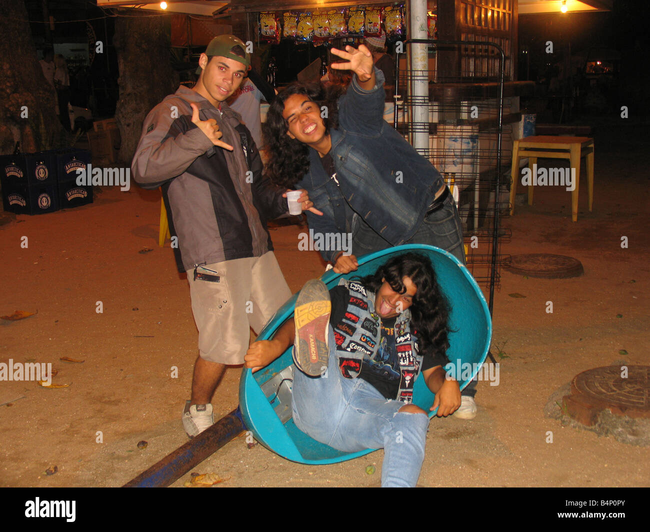 Headbangers friends on beach, one inside a phone booth with the shape of an ear, in Sepetiba Beach, Rio de Janeiro, Brazil Stock Photo