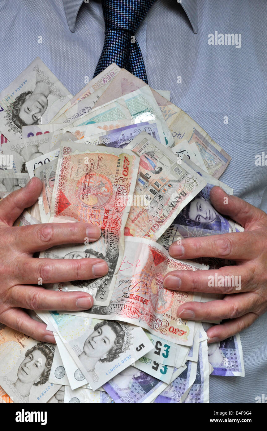 Wad of cash made up of sterling UK pound currency bank notes with hands holding money to mans chest & held by grasping fingers concept image England Stock Photo