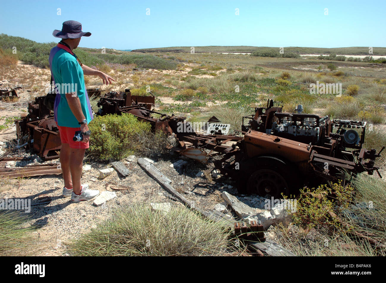 A man inspects the rusting remains of a military vehicle on Trimouille Island in the Montebello Islands of Western Australia Stock Photo