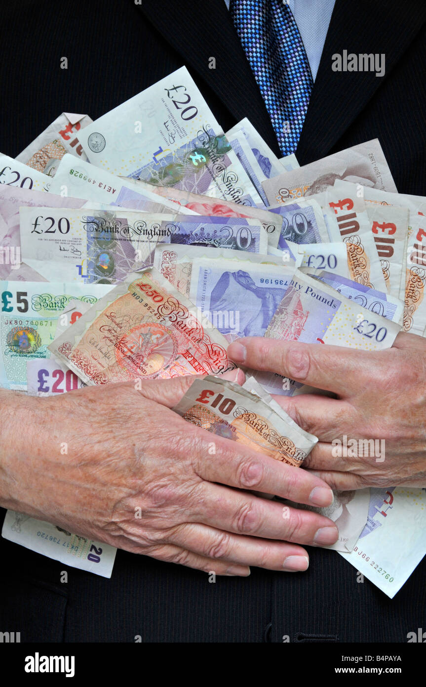 Smart man wearing office business suit with hands clutching piles of money concept for bankers, fatcats, greed, Men in Suits England UK Stock Photo