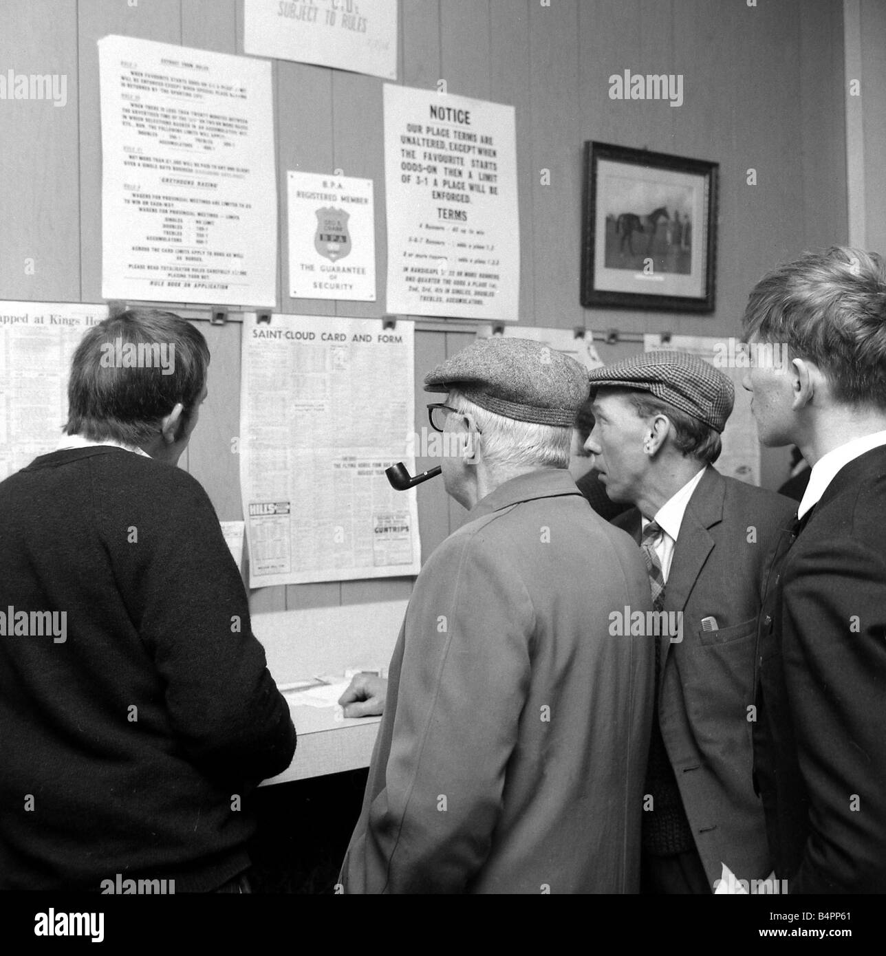 Punters studying the form guide in a French newspaper at George Crabb s betting shop before placing bets on the race at Saint Cloud in Paris October 1967 Stock Photo