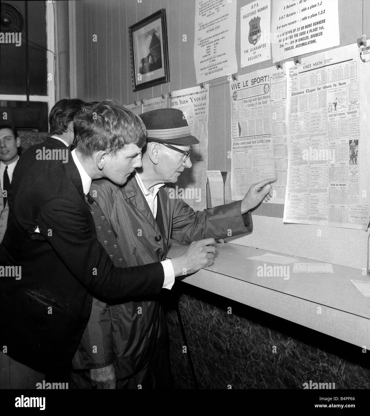 Punters studying the form guide in a French newspaper at George Crabb s betting shop in London before placing bets on the race at Saint Cloud in Paris October 1967 Stock Photo