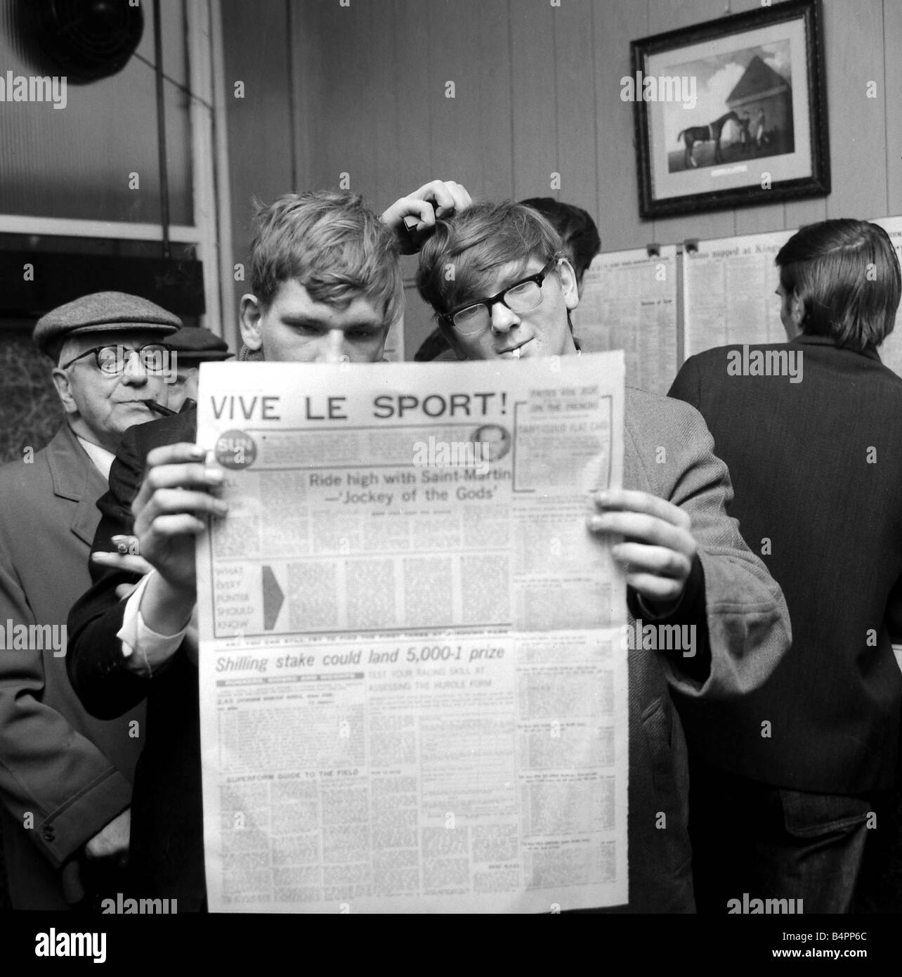 Punters studying the form guide in a French newspaper before placing their bets on the race at Saint Cloud at George Crabb s betting shop in London October 1967 Stock Photo