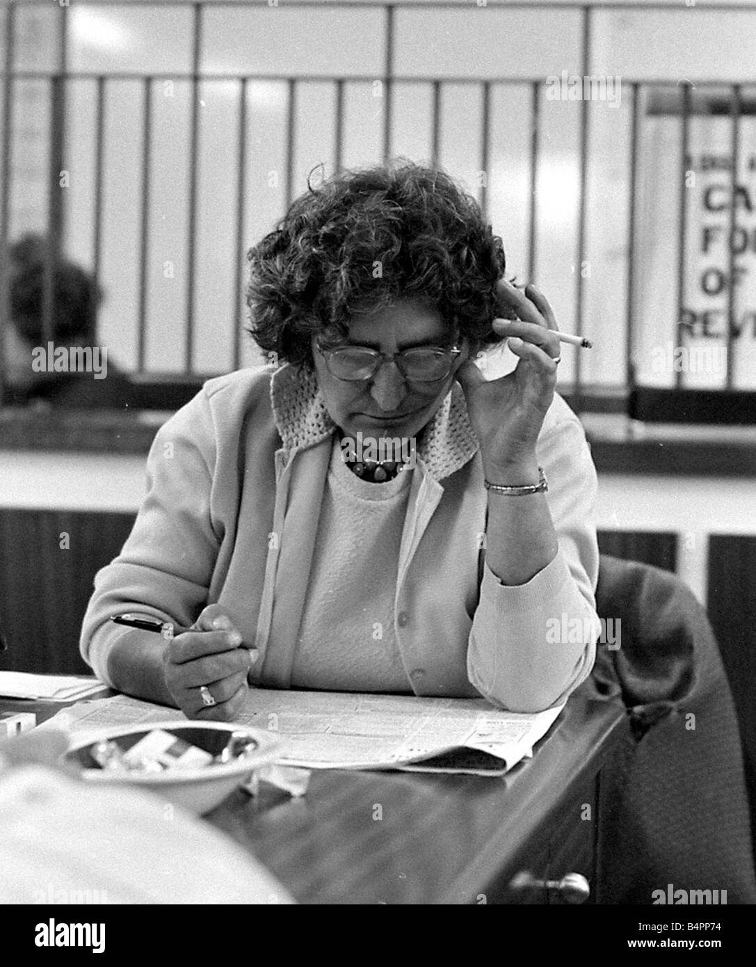 A woman smoking a cigarette as she studies the form guide before placing her bet at a Ladies only betting shop in Worcester September 1968 Stock Photo