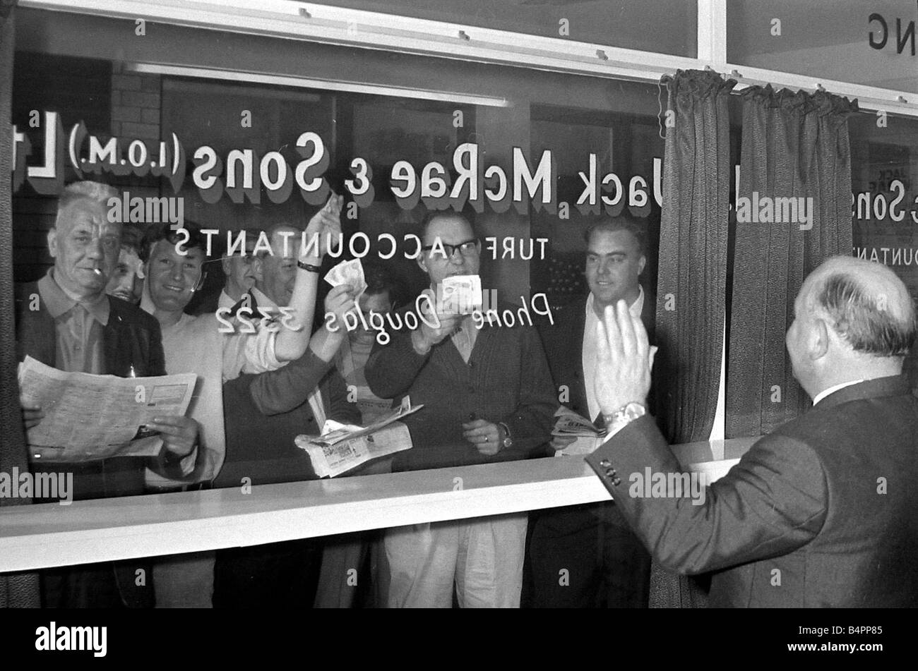 Bookmaker Sidney Glanz waves to punters waving cash at him through a glass window inside his betting shop in the Isle of Man No Stock Photo