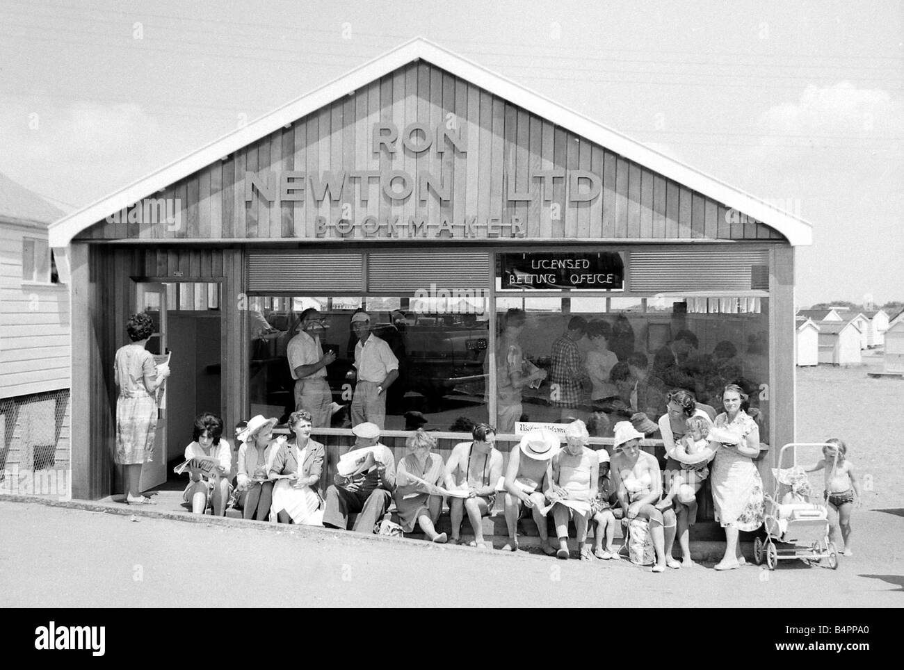 Holidaymakers enjoy the sunshine as they sit outside a betting shop in the form of a wooden chalet on the beach at Dawlish Warren in Devon July 1962 Stock Photo