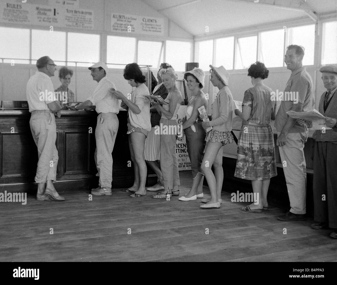 Holidaymakers line up to make a bet at a betting shop in the form of a wooden chalet on the beach at Dawlish Warren in Devon July 1962 Stock Photo