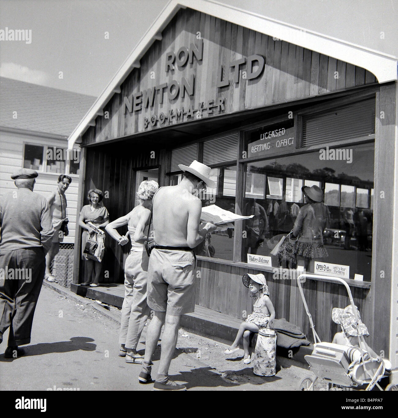 Holidaymakers study the form guide at a betting shop in the form of a wooden chalet on the beach at Dawlish Warren in Devon July 1962 Stock Photo