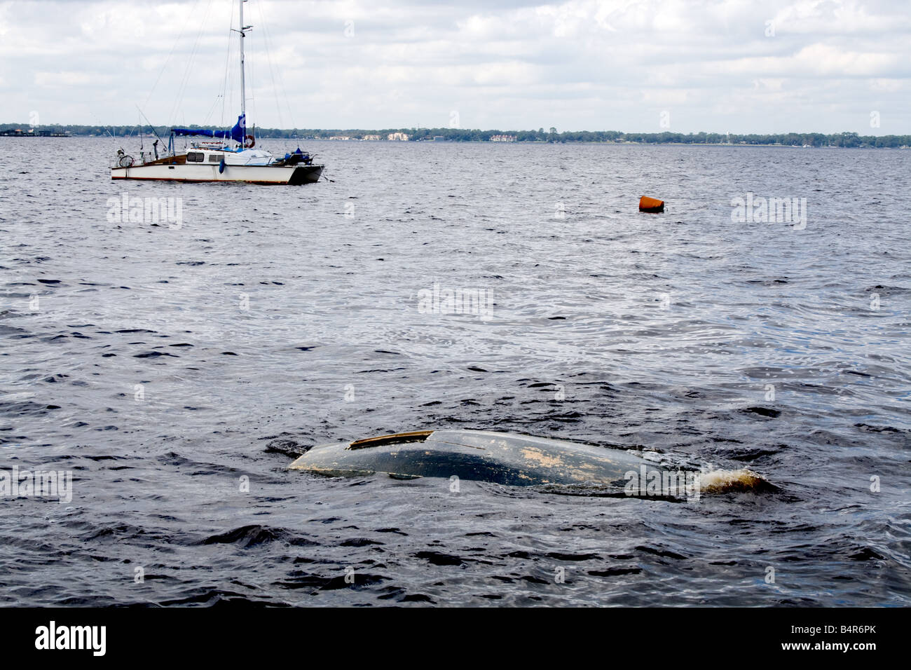 Bottom of a sunken boat almost underwater on a lake with a small sailboat in the background Stock Photo