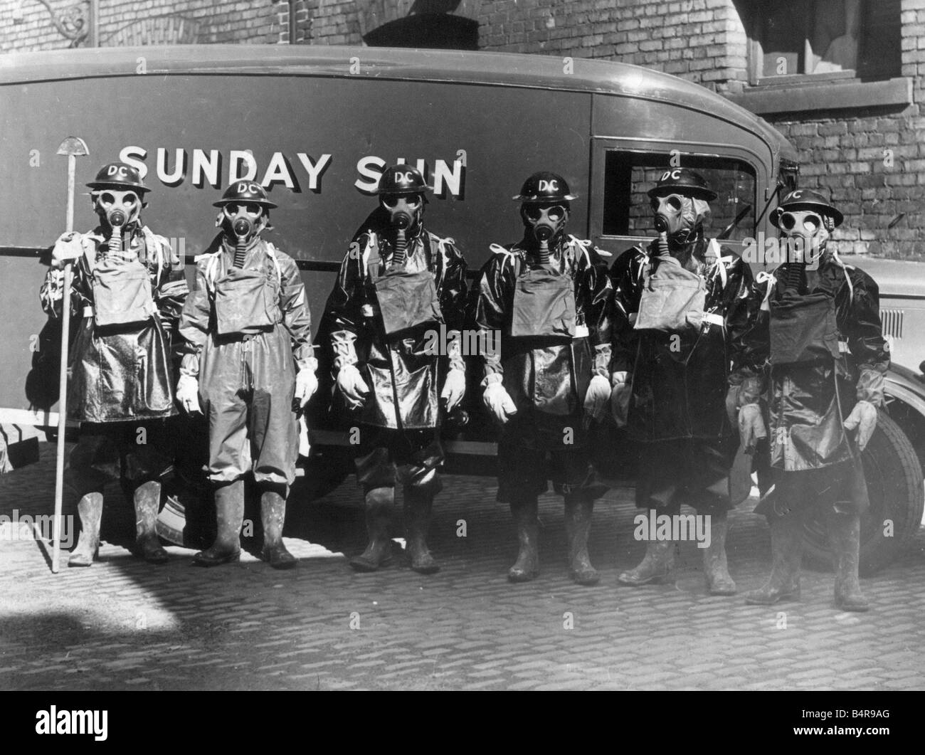 Air raid precautions Men wearing World War Two gas masks and protective clothing circa 1940 standing in front of Sunday Sun van Stock Photo