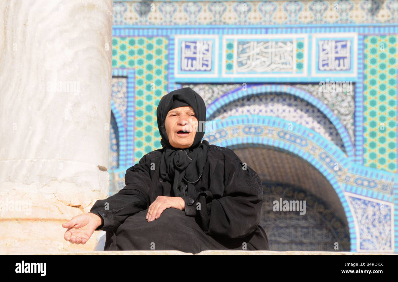 An elderly Muslim woman begs to passers-by for spare change, next to ...