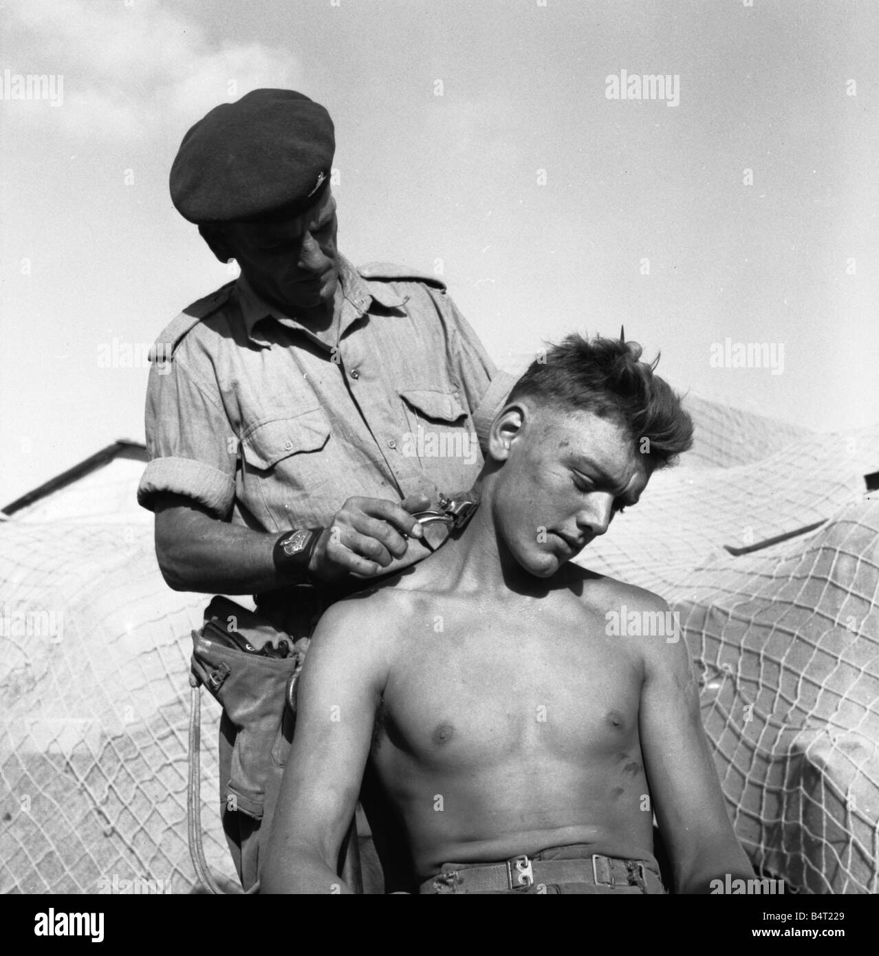 Suez Crisis 1956 Brigade Sergeant Major Ernest Lambert cuts the hair of Gunner Jim Fayers of Kings Lynn Both men belong to a Paratroop Artillery Uni which is stationed near the front line at El Cap Stock Photo