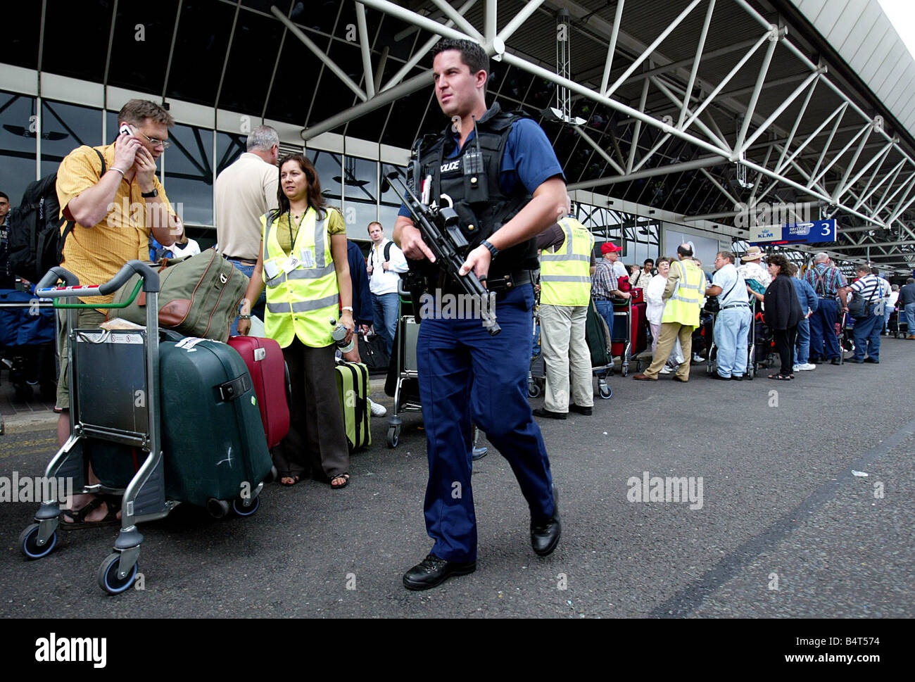 Armed police officers patrol the queues of passengers waiting outside Terminal Four at Heathrow airport where British Airways cancelled over 40 percent of its flights after the government and airport authorities brought in tougher security measures after an aborted bomb plot August 2006 Stock Photo