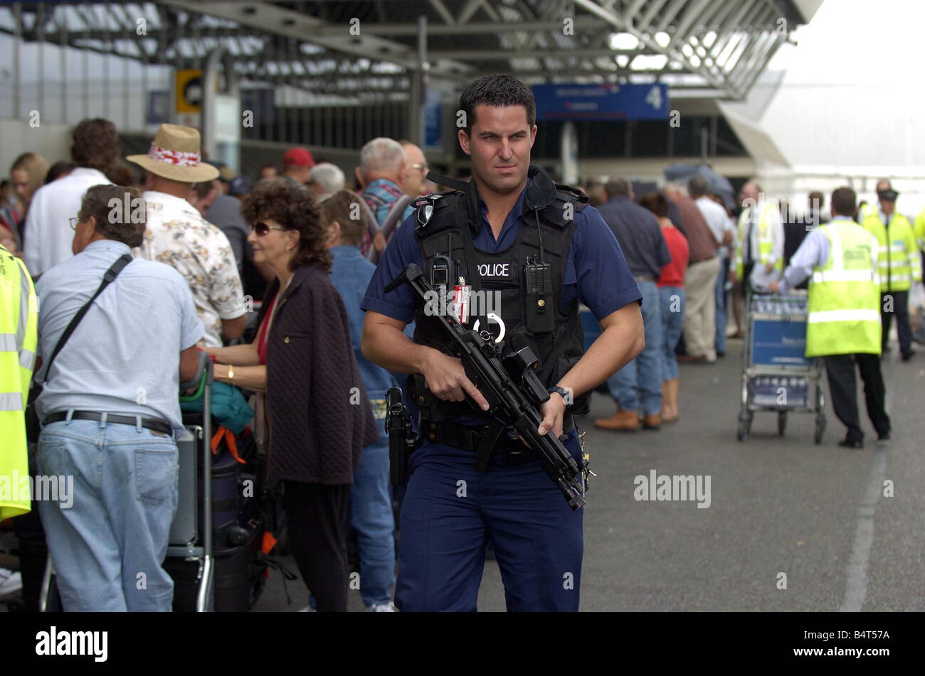 Armed police officers patrol the queues of passengers waiting outside Terminal Four at Heathrow airport where British Airways cancelled over 40 percent of its flights after the government and airport authorities brought in tougher security measures after an aborted bomb plot August 2006 Stock Photo